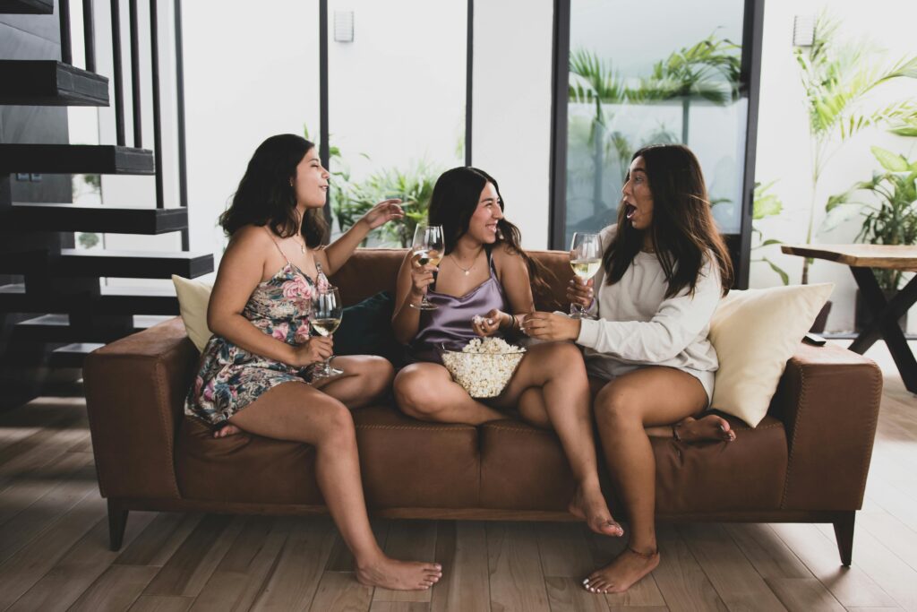 Three women enjoying each other's company on a sofa with wine and popcorn.